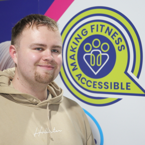 Connell, Inclusive Exercise Coach at The Angel Centre, smiling in front of Making Fitness Accessible logo