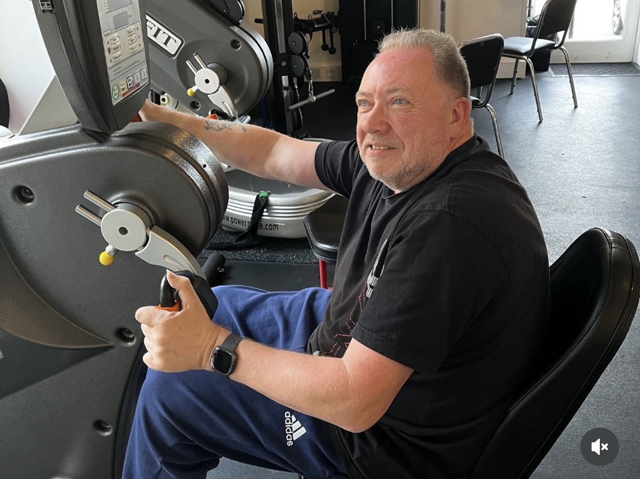 John P. using adaptive exercise equipment in the Therapy Gym, showing the supportive environment for people with neurological conditions