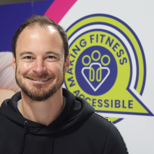 Matt Brinkley, Operations Manager and founder of Making Fitness Accessible CIC, smiling in front of Making Fitness Accessible logo